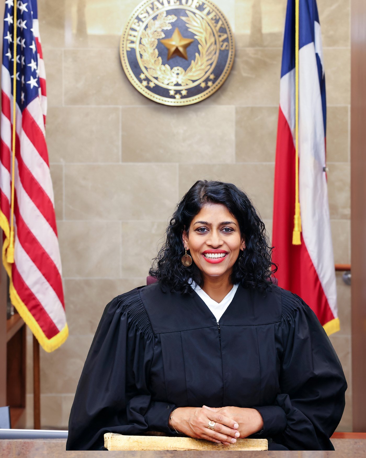 Judge Juli A. Mathew on the bench in her Fort Bend County courtroom, beneath the Seal of the State of Texas and flanked by the United States and Texas flags
